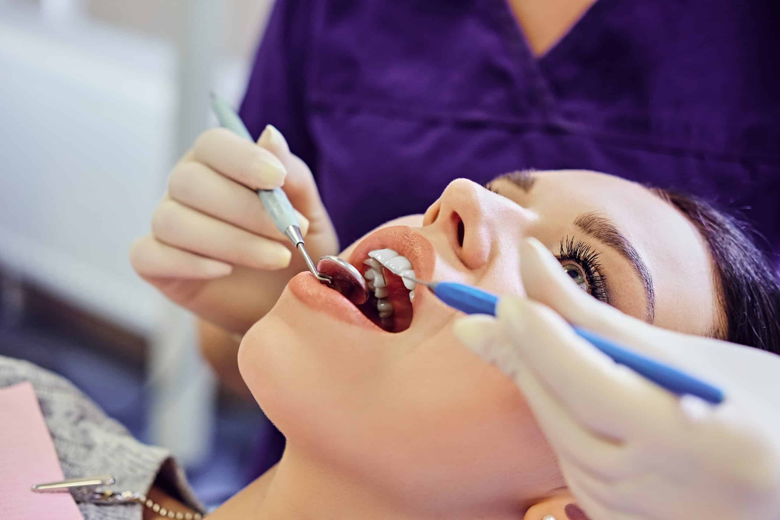 Dentist examining female’s teeth in dentistry.